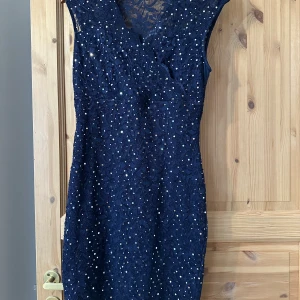 Mörkblå glittrig spetsklänning - Supersnygg mörkblå kortklänning med glittriga detaljer och spets över hela klänningen. Den har ärmlös design och en lätt transparent övre del. 