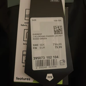 Khakigrön vindjacka från Everest - Säljer en khakigrön vindjacka från Everest med huva och hel dragkedja framtill. Jackan är vattentät, har tejpade sömmar, isolering och reflekterande detaljer. Perfekt för dig som vill ha en snygg och funktionell jacka med cool outdoor-vibe. (Aldrig använd)