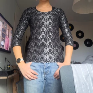 Svart spetsblus med trekvartsärm - Säljer en svart blus med genombrutet spetsmönster och trekvartsärmar. Blusen har rund halsringning och en liten knapp i nacken. Spetsen har blommigt mönster. 