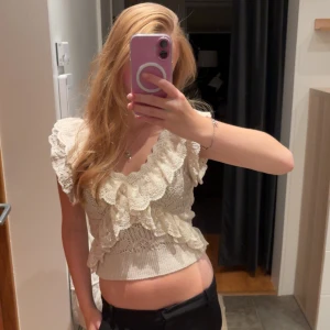 Beige spetsblus med volanger från Zara - Superfin beige blus från Zara med romantiska spetsdetaljer och volanger framtill. Croppad modell med korta ärmar och v-ringad hals. Stickad struktur och mjukt material som ger en söt vintagekänsla. Perfekt för dig som gillar detaljer och vill sticka ut. ❤️