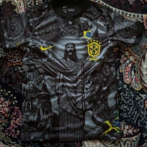 Svart Brasilien fotbollströja Nike - Unik svart Brasilien fotbollströja från Nike med detaljerat grafiskt tryck av Kristusstatyn och brasilianska symboler. Gula loggor och emblem på bröstet, korta ärmar och rund hals. Perfekt för dig som vill sticka ut på matchen eller i stan.