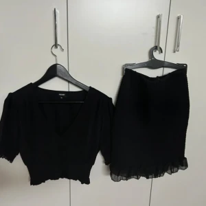 Svart kortkjol med volangkant GinaTricot - Supersöt svart kortkjol med smockad midja och volangdetalj längst ner. Kjolen har en lätt och flowy känsla, perfekt för att skapa en chic look. Enkel att matcha med olika toppar och accessoarer.