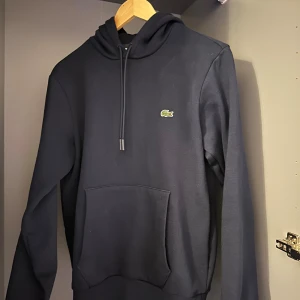 Mörkblå hoodie från Lacoste med huva - Säljer en mörk hoodie från Lacoste för endast 900 kr pris kan diskuteras box finns till.