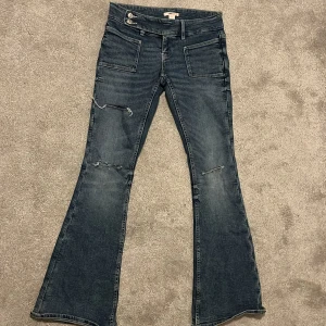 Bootcut jeans från Gina Tricot - Mörkblå bootcut jeans från Gina Tricot med slitna detaljer på benen och framsydda fickor. Jeansen har låg midja och klassisk femficksdesign. Perfekt för dig som gillar en retro vibe och vill sticka ut med en snygg siluett. Har bara använt den några få gånger. 