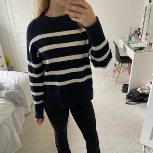 Randig stickad tröja  - Mysig stickad tröja från Stories i marinblått och vitt med breda ränder. Tröjan har långärmade ärmar, rund hals och en cool slitsdetalj på båda sidor. Ribbstickade muddar vid ärmslut och nederkant. 