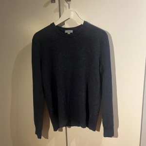 Yak-ull tröja från COS - Snygg mörkblå stickad tröja från COS i storlek L. Tröjan har rund halsringning, ribbade muddar och långärmad passform. Perfekt för dig som gillar enkel och stilren design med en chill vibe. 25% yak-ull. Har en liten lagning på armen, men inget som märks vid användning.