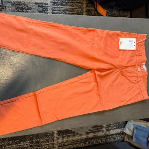 Orange chinos från Manuel Ritz, strl 48 - Snygga orange chinos från Manuel Ritz i storlek 48. Byxorna har raka ben, klassisk knappstängning och fickor både fram och bak. Tillverkade i mjuk bomull med en fräsch och modern look som sticker ut.