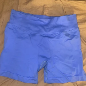 Blå tighta träningsshorts - Säljer ett par blå tighta träningsshorts med hög midja och bred resår. De är stretchiga och sitter skönt på kroppen, perfekta för gymmet eller löprundan. Materialet känns mjukt och följsamt mot huden.