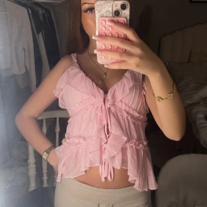 Rosa volang blus med knyt - Supersöt ljusrosa blus med volanger och snörning framtill vilket gör den justerbar. Den är i storlek M men passar mig som vanligtvis har XS! Knappt använd, alltså nyskick💓