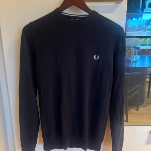 Svart tröja från Fred Perry - Säljer en svart långärmad tröja från Fred Perry med klassisk rund hals och den ikoniska loggan broderad på bröstet. Tröjan är i mjuk bomull och har en stilren, enkel design som passar perfekt till jeans eller chinos.