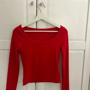 Röd långärmad topp med rund hals - Snygg röd topp med lång ärm och rundad halsringning. Modellen är figurnära och har en enkel, stilren design utan mönster eller detaljer. Perfekt för dig som gillar färgstarka och klassiska plagg. Materialet känns mjukt och stretchigt.