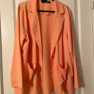 Persikofärgad kavaj från Bik Bok - Snygg persikofärgad kavaj från Bik Bok i storlek S. Kavajen har klassisk krage, två stora fickor framtill och stängs med en knapp. Långärmad och i ett lätt, slätt material som känns skönt mot huden. Perfekt för dig som vill sticka ut med färg.