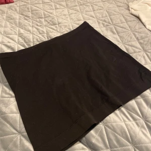 Svart kortkjol från H&M Basic - Enkel och stilren svart kortkjol från H&M Basic. Kjolen har rak passform och är tillverkad i ett mjukt bomullsmaterial som gör den bekväm att bära. Perfekt att matcha med en crop top eller oversized hoodie.