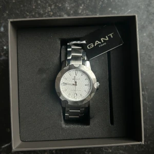 GANT St.Claire Silver Metal klocka - Aldrig använd helt ny och äkta! Box kommer med! Skriv om ni har frågor eller mått! Snygg GANT St.Claire klocka i silverfärgat metall med länkarmband och rund boett. Urtavlan är vit med ett vågigt mönster och tydliga markeringar. Låset har GANT-logga och hela klockan har en stilren vibe som passar till alla outfits. 🥰