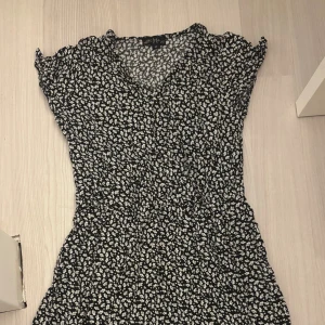 Svart blommig kortklänning - Supersöt svart kortklänning från XOXO by Frias (gekås Ullared) med vitt blommönster. Klänningen har v-ringning, korta ärmar och lätt volang i nederkanten. Perfekt för dig som gillar en feminin och trendig stil. Pris kan diskuteras!