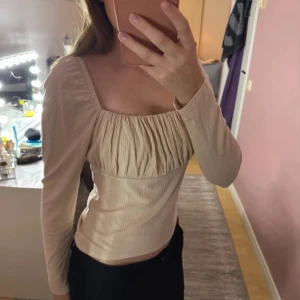 Beige ribbad blus med rynkad front - Säljer en beige blus med lång ärm och fyrkantig urringning. Storlek M passar även S