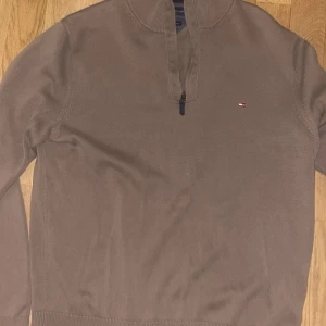 Beige half zip tröja Tommy Hilfiger - Snygg beige långärmad tröja från Tommy Hilfiger med half zip och liten broderad logga på bröstet. Tillverkad i premium bomull, perfekt för dig som gillar stilrena och klassiska plagg. Ribbad vid krage och muddar för extra komfort.