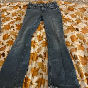 Blå bootcut jeans från Mavi Jeans Co. - Snygga blå jeans från Mavi Jeans Co. med klassisk bootcut passform och slitna detaljer. Jeansen har fem fickor, bälteshällor och dragkedja med knapp. Materialet är robust denim och färgen är ljusblå med tvättad look.