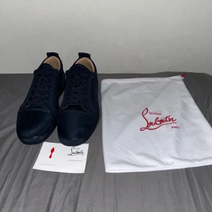 Mörkblå mocka sneakers Christian Louboutin - Snygga mörkblå sneakers från Christian Louboutin i lyxig mocka med klassisk rund tå och snörning. Skorna har den ikoniska röda sulan med Louboutin-logga undertill. Perfekta för dig som vill sticka ut med exklusiv stil. Skorna har använts en gång därmed har dom små skråmor på sulan därefter kommer priset. Allt i första bilden följer med. Är de några frågor är de bara att skriva.