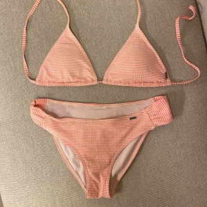 Rosa- och vitrandig bikini med snören - Bikini från märket Firefly. Lappen är tyvärr bortklippt så jag kan tyvärr inte se storleken. Skulle uppskatta på kanske storlek 36, men det är svårt att säga. Använd men välfungerande:)