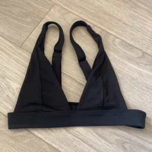 Svart ribbad linne-topp - Säljer en svart ribbad linne-topp med bred resår nedtill och justerbara axelband. Toppen har en enkel och stilren design med triangelformade kupor, perfekt att styla till olika outfits.