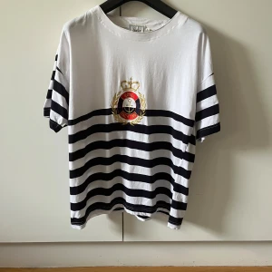 Randig t-shirt från Sinclair KappAhl strl L (42/44) - Vit och marinblå randig t-shirt från Sinclair KappAhl med broderad Royal Yachting-logga på bröstet. Klassisk passform, kortärmad och tillverkad i 100% bomull. Storlek L (42/44)