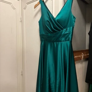 Balklänning - En jättevacker emeraldgrön siden balklänning med v ringning i storlek 38. Endast använd en gång men har skador på kjolen som ej syns på långt håll. Köpt för 2500kr
