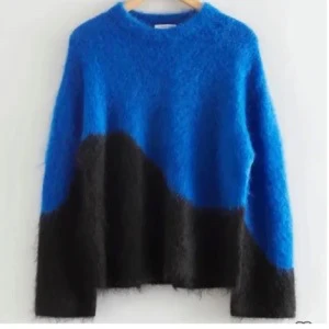 Blå och svart fluffig stickad tröja - Säljer en riktigt snygg stickad tröja i blått och svart med coolt grafiskt mönster ifrån &otherstories. Tröjan är fluffig och har långärmade, loose passform. Perfekt för dig som gillar att sticka ut med färg och mjukt material.