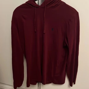 Ralph Lauren Hoodie - Säljer denna Ralph Lauren hoodie i väldigt fint skick. Det är en hoodie med tunt material och en snygg vinröd färg som passar perfekt till hösten. Hoodien är svår att hitta och är perfekt för en avslappnad lager på lager look.