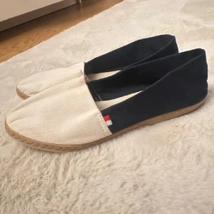 Tommy Hilfiger blåvita espadrillos - Snygga espadrillos från Tommy Hilfiger i marinblått och vit bomullstyg. Skorna har klassisk flätad sula och en liten rödvit detalj vid sidan. Perfekta för sommaren med sin lätta och luftiga känsla.
