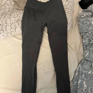 Mörkgrå leggings från Relode - Säljer ett par mörkgrå leggings från Relode med hög midja och diskret scrunch-detalj bak. De är stretchiga och sitter tight, perfekta för gymmet eller chill. Materialet är mjukt och följsamt för maximal komfort.
