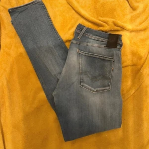 Replay anbass 34 - Snygga blå jeans från Replay med en klassisk femficksdesign. Jeansen har en lätt tvättad look och är perfekta för en avslappnad stil. De har en knappgylf och bälteshällor för extra funktionalitet.