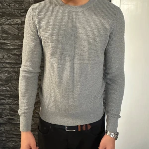 Grå stickad tröja från J.Lindeberg - Säljer en stilren grå stickad tröja från J.Lindeberg. Tröjan har rund halsringning, långärmad design och ett snyggt strukturerat mönster. Perfekt för lager-på-lager och funkar året runt. Passar dig som gillar klassisk men modern stil. Köpt på Åhléns , Nypris : 1000kr