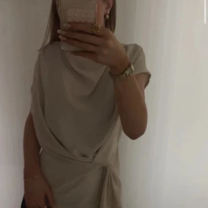 Beige omlottklänning med knyt - Säljer en stilren beige omlottklänning med knyt i midjan och korta ärmar. Klänningen har en mjuk, draperad look och passar perfekt för dig som gillar minimalistisk stil. Superfin till smycken och accessoarer.