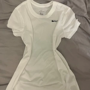 Vit Nike t-shirt med svart logo - Aldrig använd!!! Fräsch vit t-shirt från Nike med klassisk svart swoosh på bröstet. T-shirten har rund halsringning och korta ärmar. Tillverkad i mjukt material som känns skön mot huden. Perfekt för en sportig och clean look. 