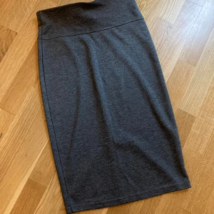 Mörkgrå pennkjol i bomull - En stilren mörkgrå pennkjol i mjukt bomullsmaterial. Kjolen har hög midja och en diskret slits bak för extra rörelsefrihet. Enkel och clean design som är lätt att matcha med olika toppar och sneakers eller boots. Stl:34/36.  Aldrig använd. Köpt på Sisters