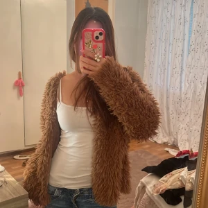 Brun teddyjacka från Gina Tricot - Supermysig brun teddyjacka från Gina Tricot i storlek L. Jackan har fluffig pälslook, långärmad och är fodrad på insidan för extra komfort. Perfekt för dig som vill ha en chill och trendig vibe. Snygg att styla med jeans eller kjol!