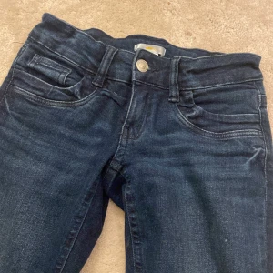 Mörkblå bootcut jeans - Mörkblå jeans med klassisk femficksdesign och bootcut-ben. Jeansen har normal midja och är tillverkade i ett mjukt denimtyg som ger en snygg passform. Perfekta för dig som gillar en tidlös och avslappnad stil.