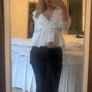 Vit omlottblus med volangdetaljer - Säljer en vit omlottblus med v-ringning och volangdetaljer på axlarna. 
