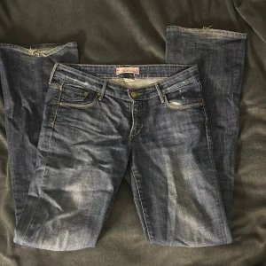 Blå jeans från &Star  - Snygga blå jeans från &Star med klassisk femficksdesign och guldfärgade detaljer. Jeansen är bootcut och är tillverkade i slitstarkt denimtyg med lätt tvättad look. Perfekta för en avslappnad stil.