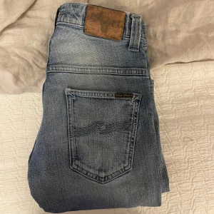 Nudie Jeans Thin Finn Indigo Fusion - Slimmade och snygga jeans från Nudie Jeans, modellen Thin Finn Indigo Fusion. Färgen är ljusblå med tvättad look och klassiska detaljer som fem fickor och bruna nitar. Materialet är 98% ekologisk bomull och 2% elastan för extra stretch och komfort.storlek 29 32 modell thin Finn