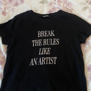 T-shirt med tryck  - Svart t-shirt från Tally Weijl med vit text 'BREAK THE RULES LIKE AN ARTIST' på framsidan. Klassisk rund hals och korta ärmar. Mjuk och skön bomullskvalitet, perfekt för dig som gillar statement-plagg och enkel stil. Bra i storlek. Sälja pga ingen använding.