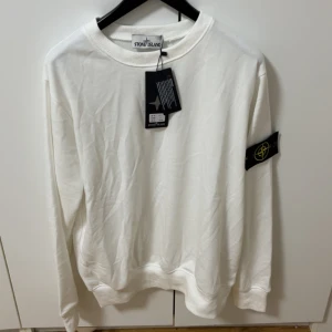 Vit sweatshirt från Stone Island - Vit sweatshirt från Stone Island med klassisk rund hals och ribbade muddar. Tröjan har lång ärm och den ikoniska Stone Island-loggan på vänster ärm. Mjuk bomullskvalitet som känns skön mot huden och passar perfekt till en clean streetwear-look.den är strl S tar byten beror på vad det är och pris kan alltid diskuteras. helt ny aldrig använd 