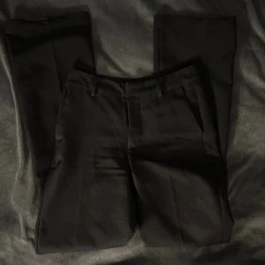 Svarta kostymbyxor från BikBok - Snygga svarta kostymbyxor från BikBok i storlek 34. Klassisk rak modell med pressveck, hällor för bälte och två bakfickor. Perfekta för en clean och stilren look. Modellen heter PW Vilma.