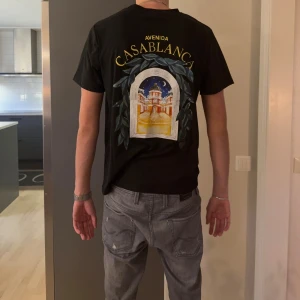 Svart Casablanca t-shirt med tryck - Svart t-shirt från Casablanca med färgglatt tryck av en byggnad och texten 'Avenida Casablanca' på ryggen. Mindre tryck på bröstet. Klassisk passform och rund hals. Perfekt för dig som gillar streetwear med unik design.
