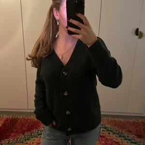 Grön stickad kofta med knappar - Mysig grön kofta med v-ringning och stora knappar framtill. 