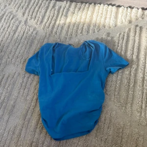 Blå topp med fyrkantig ringning från Zara - Säljer en blå topp från Zara med korta ärmar och snygg fyrkantig ringning. Toppens material är mjukt och stretchigt, perfekt för en trendig look. Enkel att matcha med både jeans och kjol. Färgen är klarblå och modellen är figurnära.