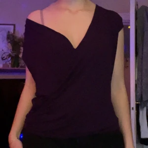 Mörklila omlottopp Gina Tricot - Snygg mörklila omlott topp från Gina Tricot i storlek M. Toppen har en djup v-ringning och är ärmlös med en loose passform. Materialet är mjukt och stretchigt, troligen bomull eller polyester. Perfekt för dig som gillar stilrena och trendiga plagg.