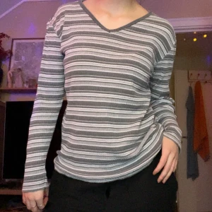 Randig långärmad tröja från Lipp - Grå och vit randig långärmad tröja från Lipp med v-ringad hals. Tröjan har en ribbad struktur och normal passform, perfekt för dig som gillar en chill och enkel stil. Snygg att matcha med jeans eller mjukisbyxor. Vintage etikett.