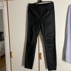 Svarta byxor från Vila, stl L - Svarta byxor från Vila i storlek L. Byxorna har klassisk femficksdesign, bälteshällor och dragkedja med knapp. Materialet har en lätt glansig finish som ger en cool look. Perfekta för dig som gillar en tight och stilren stil.